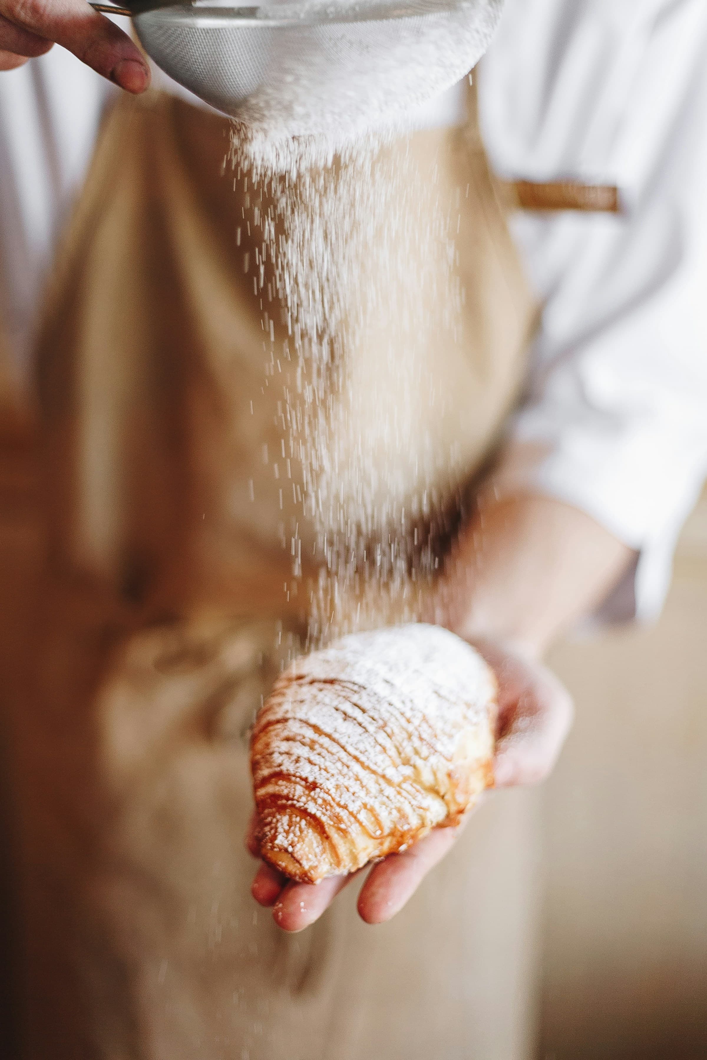 Baker carefully dusting a golden croissant with powdered sugar