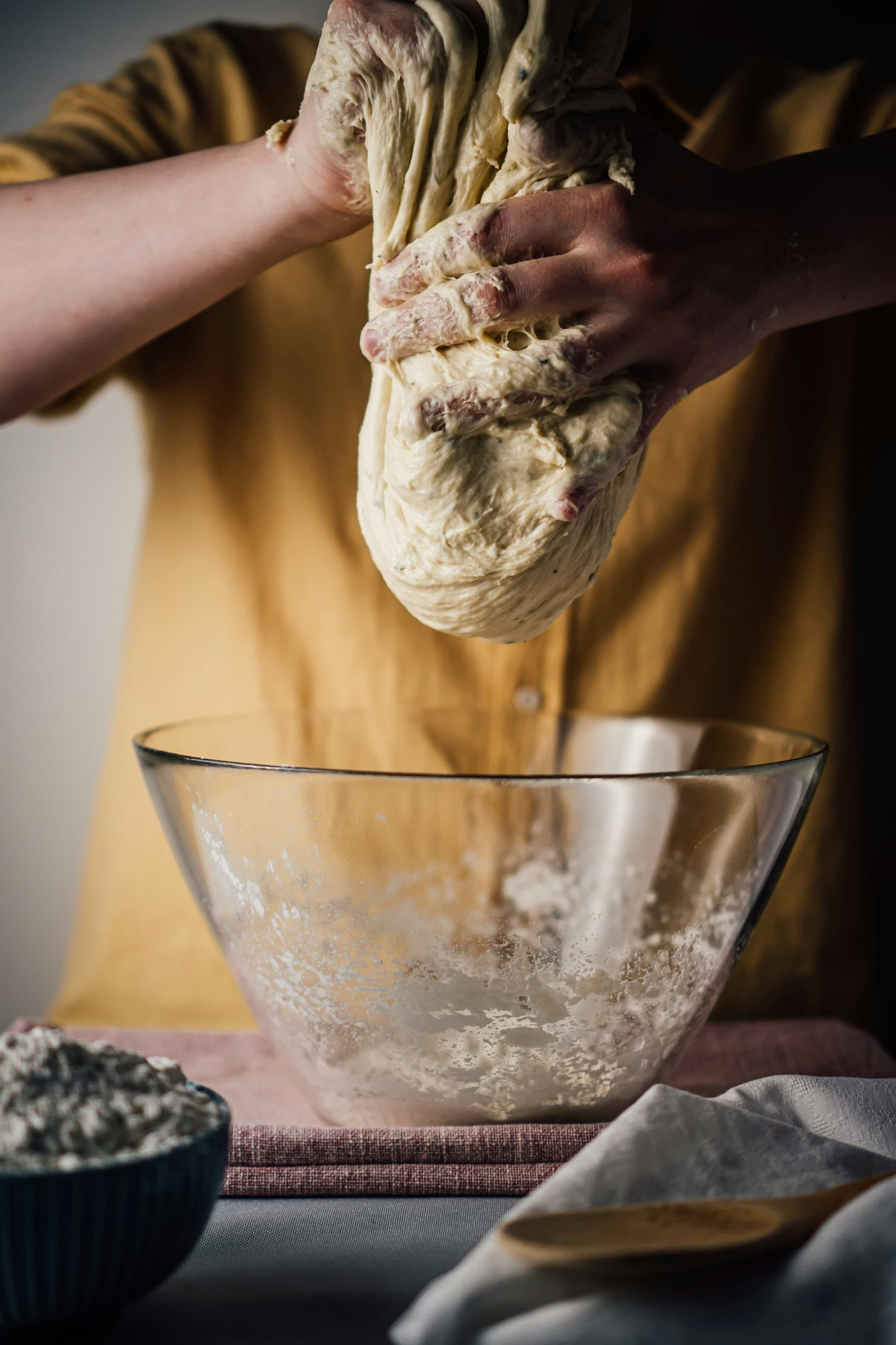 Baker kneading dough over a glass mixing bowl